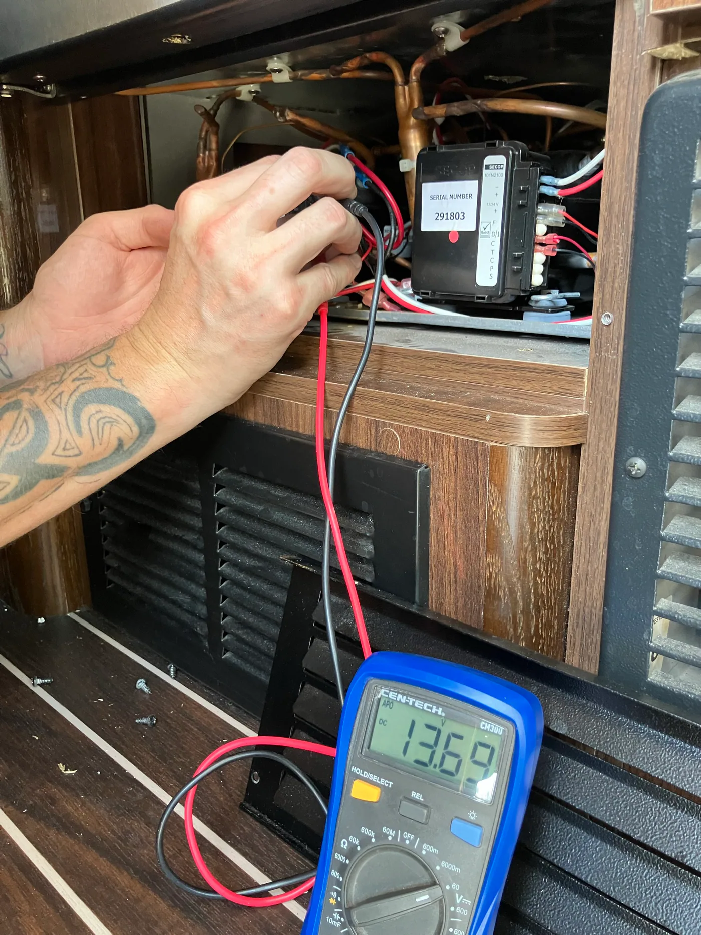 Multimeter measuring 13.69 volts at a SECOP 12-volt refrigerator compressor controller