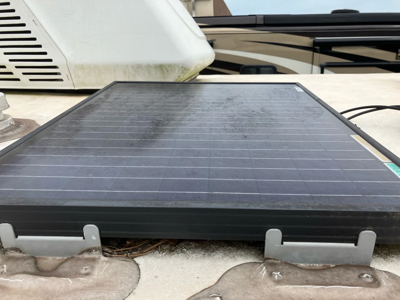 Dusty solar panel mounted on an RV roof beside an air conditioner