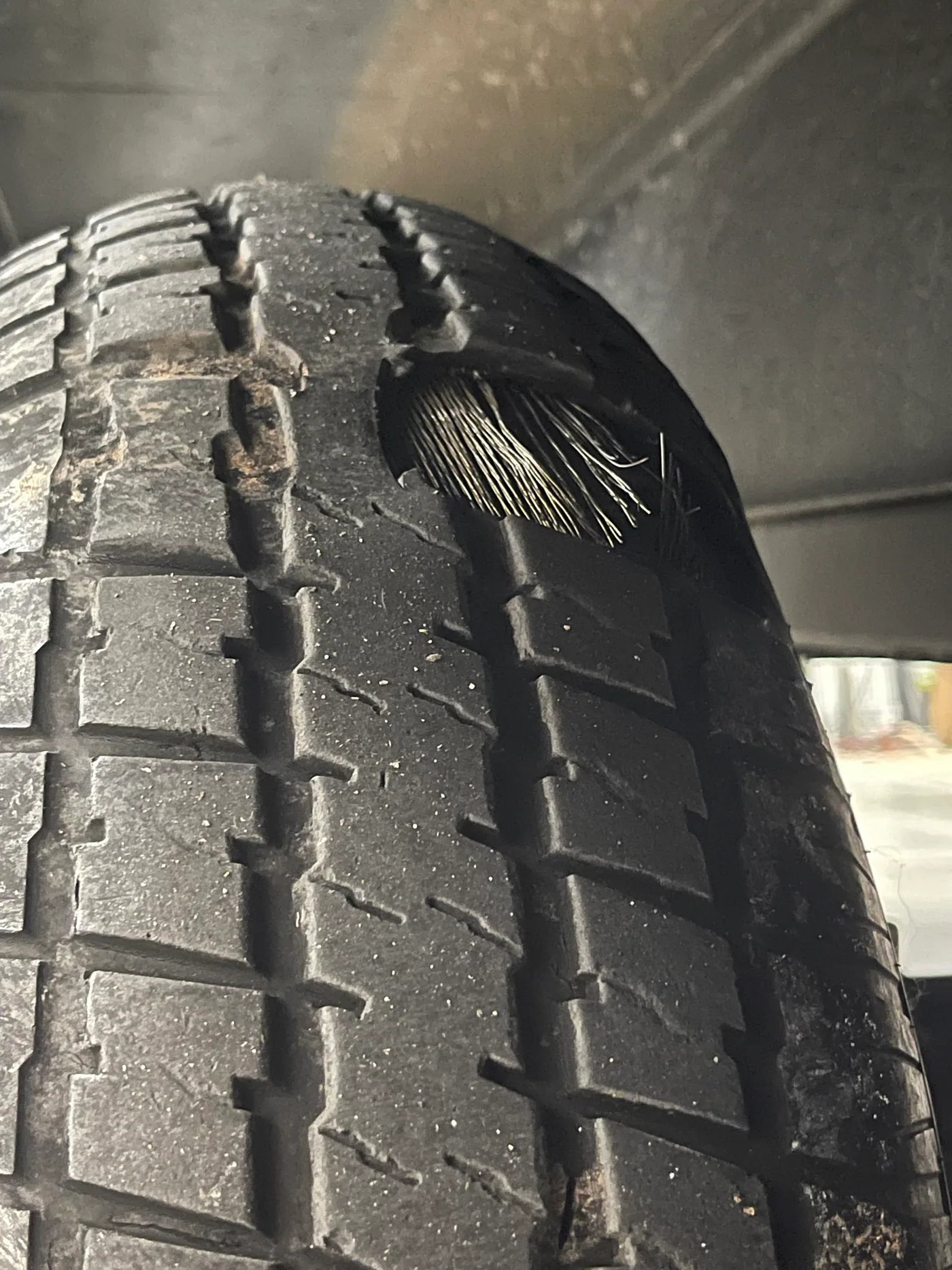 RV trailer tire with steel belt cords exposed through a damaged tread shoulder